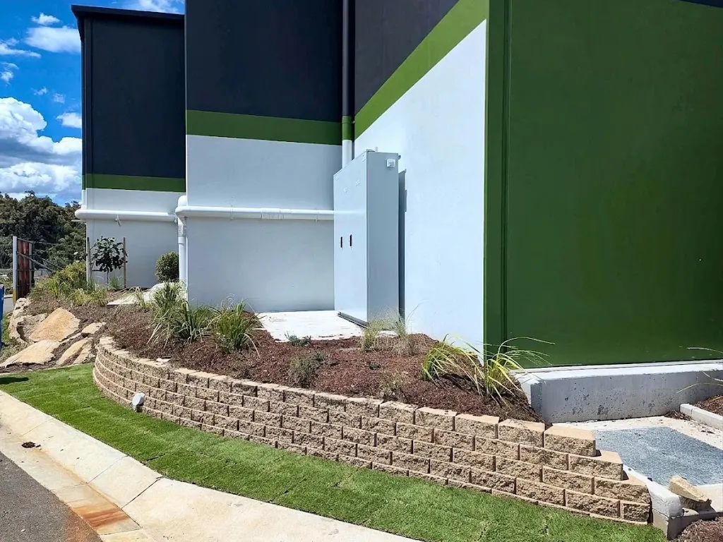 Curved block retaining wall with new turf and planting beside a commercial building