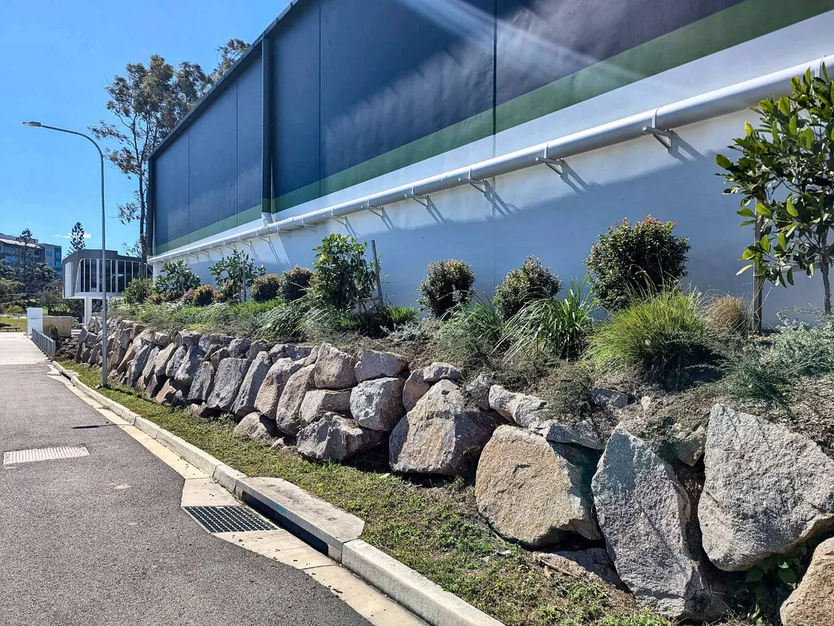 Rock retaining wall with new planting above a roadside kerb