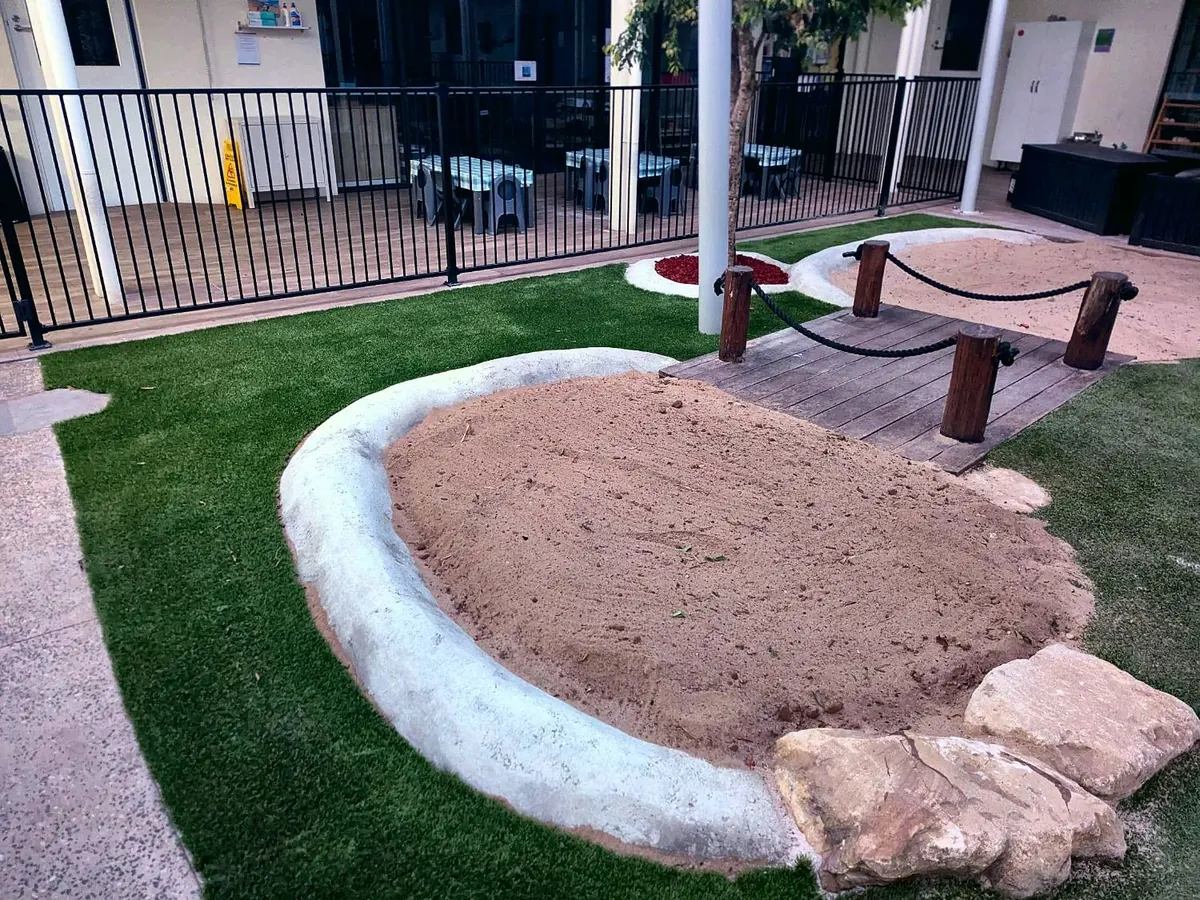 Rebuilt sandpit with a curved edge, timber bridge and synthetic turf