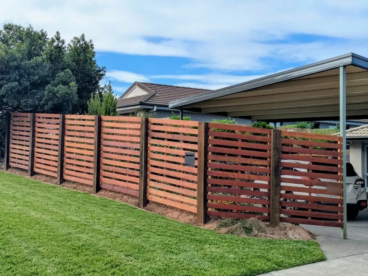 Horizontal slat timber fence with hardwood posts along a front lawn beside a carport